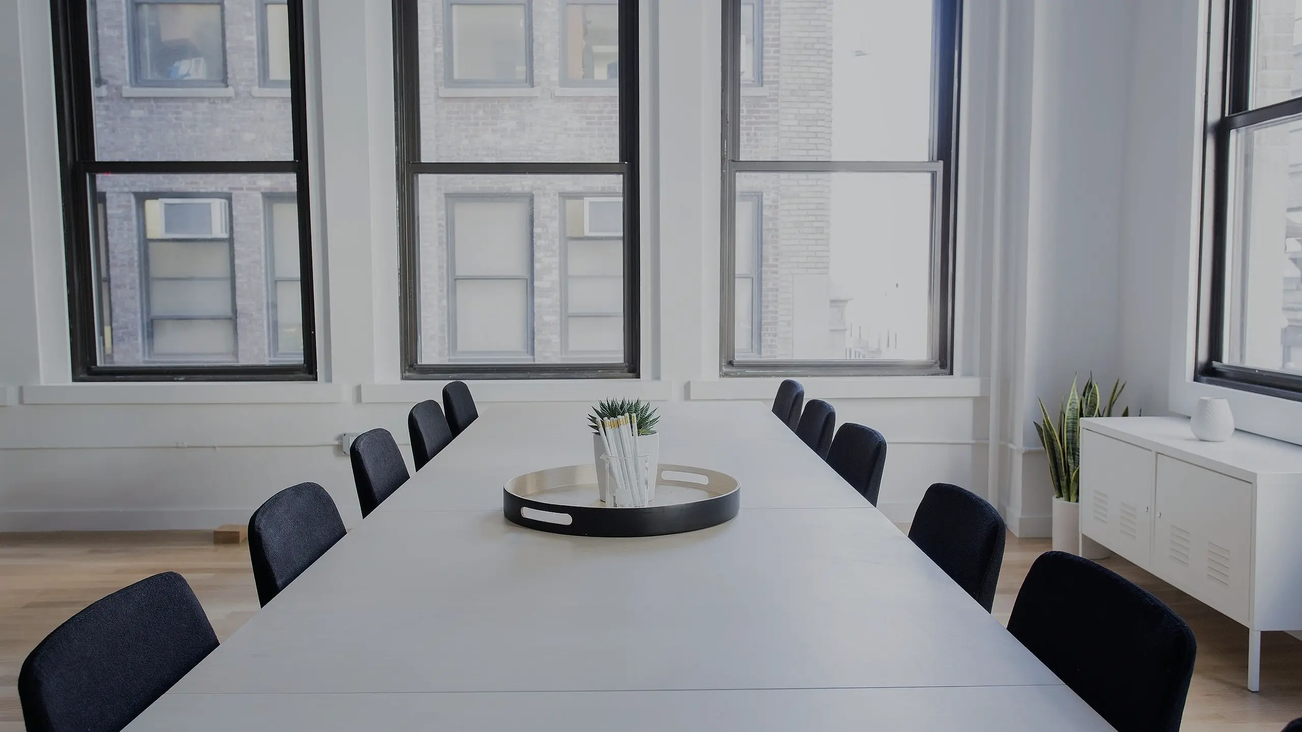 Salle de réunion minimaliste, longue table blanche et fenêtres à châssis noirs de plancher à plafond