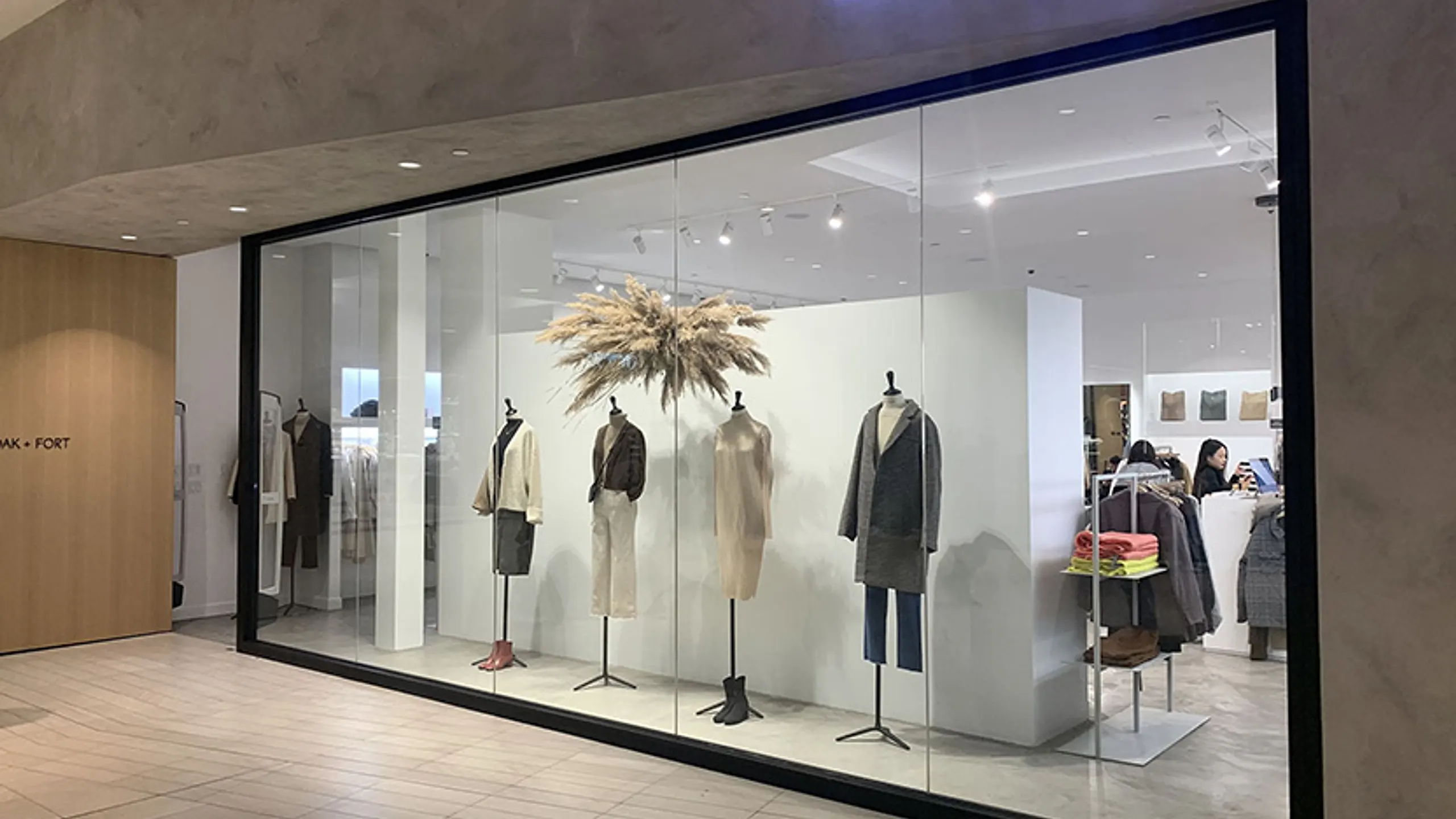Vitrine de boutique haut de gamme Oak + Fort : verre transparent laissant voir les collections exposées sur mannequins, puis verre opaque PDLC activé pour la confidentialité nocturne